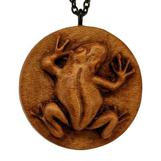 Wooden pendant necklace carved in the shape of a frog. Made from hard maple wood and hanging from a black stainless steel chain against a white background.