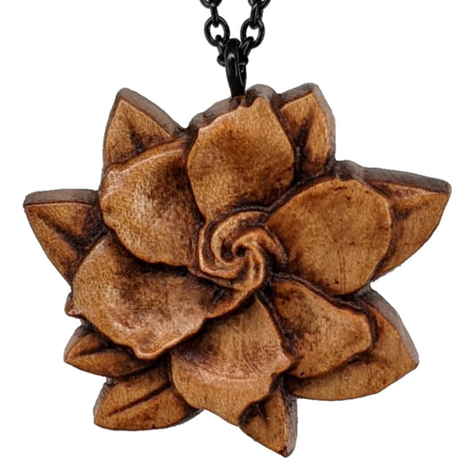 Wooden flower necklace pendant carved in the shape of a gardenia against. Made from hard maple and hanging from a black stainless steel chain against a white background.