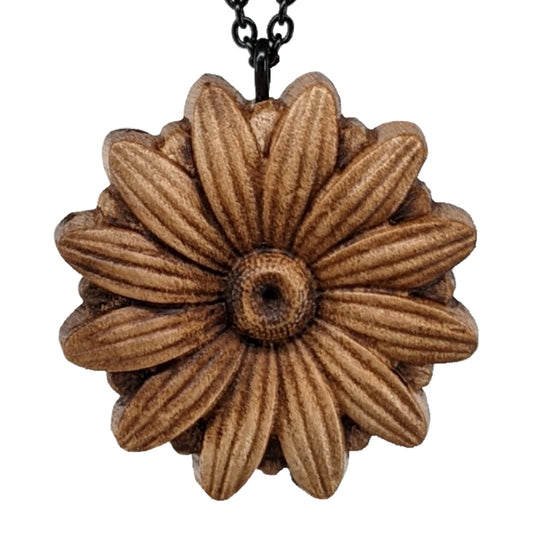 Wooden necklace pendant carved into the shape of a daisy flower. Hanging from a black stainless steel chain against a white background.