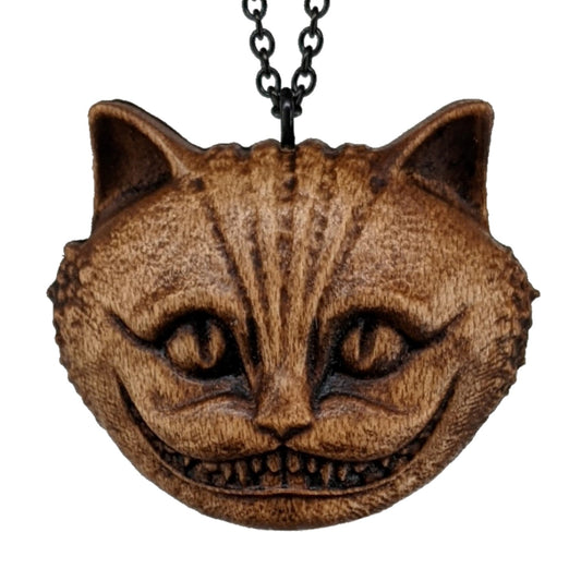 Wooden necklace pendant carved in the shape of a Cheshire cat head. Hanging from a black stainless steel chain against a white background.
