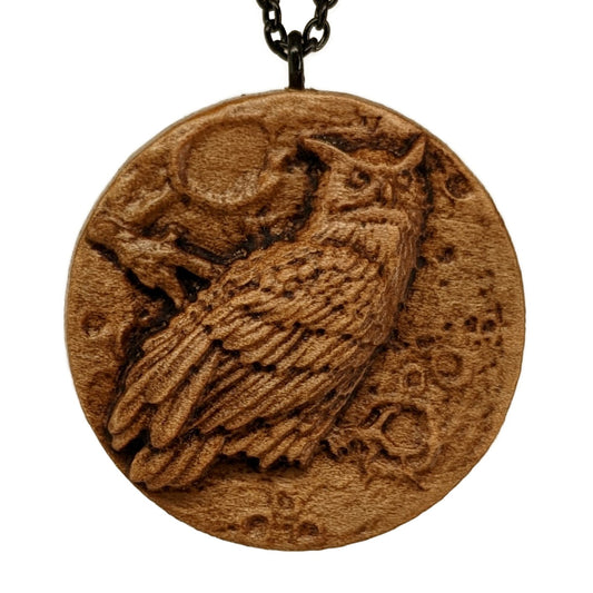 Round wooden necklace pendant carved in the shape of an owl against a full moon. Made from hard maple and hanging from a black stainless steel chain against a white background.