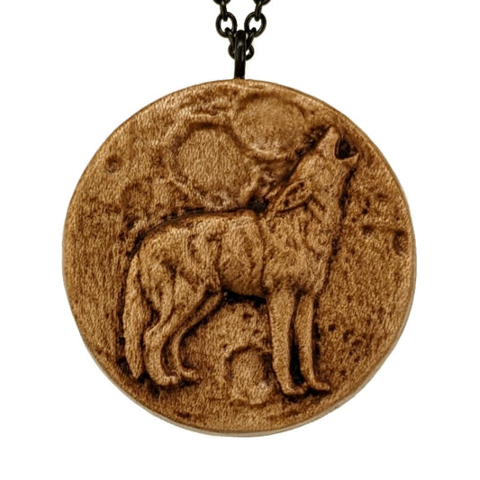 Wooden necklace pendant depicting a howling wolf in front of a full moon. Carved in a realistic style from hard maple wood. Hanging from a black stainless steel chain against a white background.
