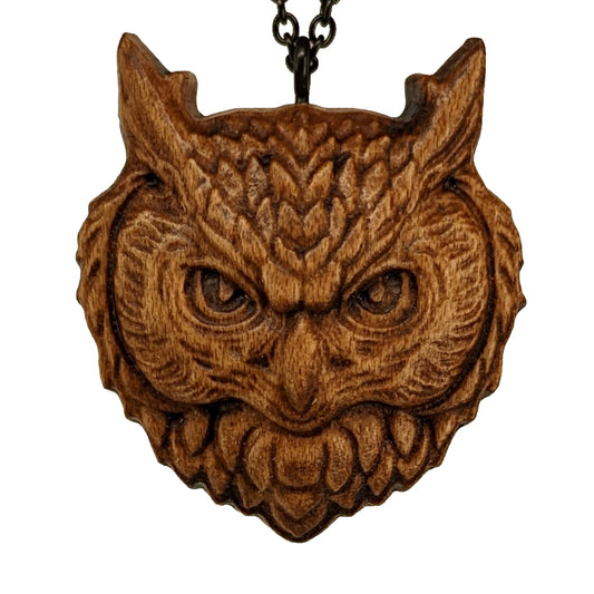 Wooden necklace pendant carved in the shaped of an owls head. Made from hard maple wood. Hanging from a black stainless steel chain against a white background.