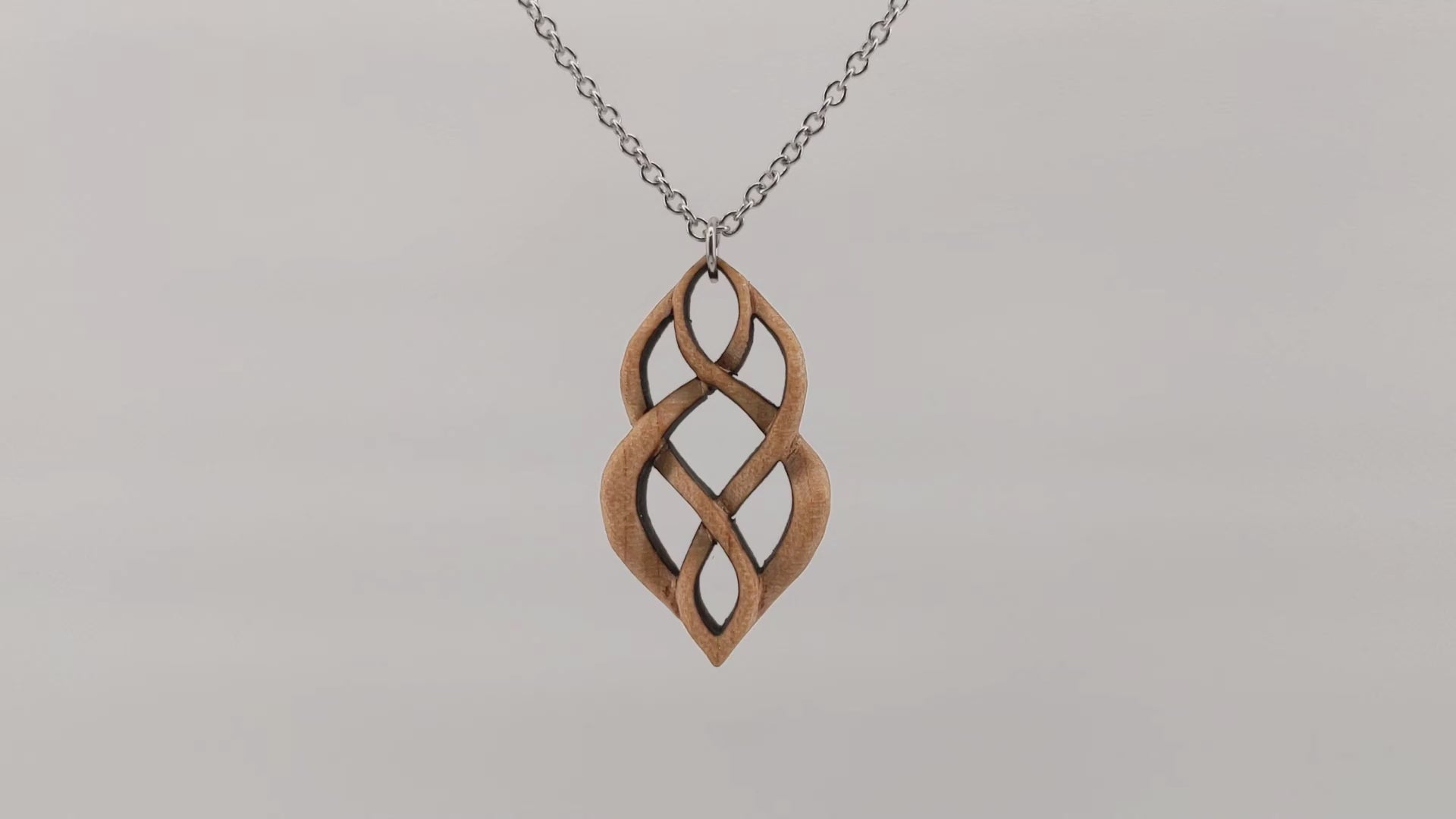 Wooden necklace pendant carved so that curving shapes weave into each other. Made from hard maple wood. Hanging and rotating from a black stainless steel chain against a white background.