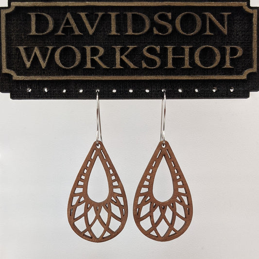 Pair of wooden earrings with silver stainless steel hooks. They are brown teardrop shaped with a woven pattern within and a tear in the center. Made from birch wood hanging from a model Davidson Workshop sign against white background.(Close up View)