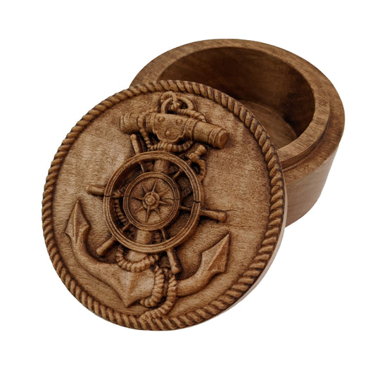 Round wooden box 3D carved with a ship anchor wrapped in rope that leads out to a rope border. There is a ship wheel in the anchors center with a compass emblem in its center. Made from hard maple wood with a brown stain against a white background.
