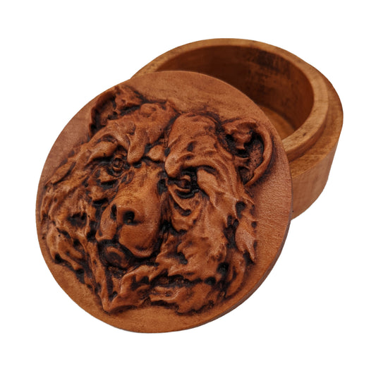 Round wooden box 3D carved with a bears head looking straight ahead. It has burly fur and a forrrowed brow and mouth shut, giving off a stern expression. Made from hard maple wood with a brown stain against a white background.
