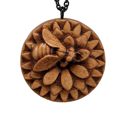 Wooden necklace pendant carved in the shape of a honey bee resting on a flower. Made from hard maple wood and hanging from a black stainless steel chain against a white background.