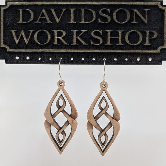Pair of wooden earrings with silver stainless steel hooks. They are diamond shaped woven patterned carvings with inner diamonds woven within. Made from hard maple hanging from a model Davidson Workshop sign against a white background. (Close up View)