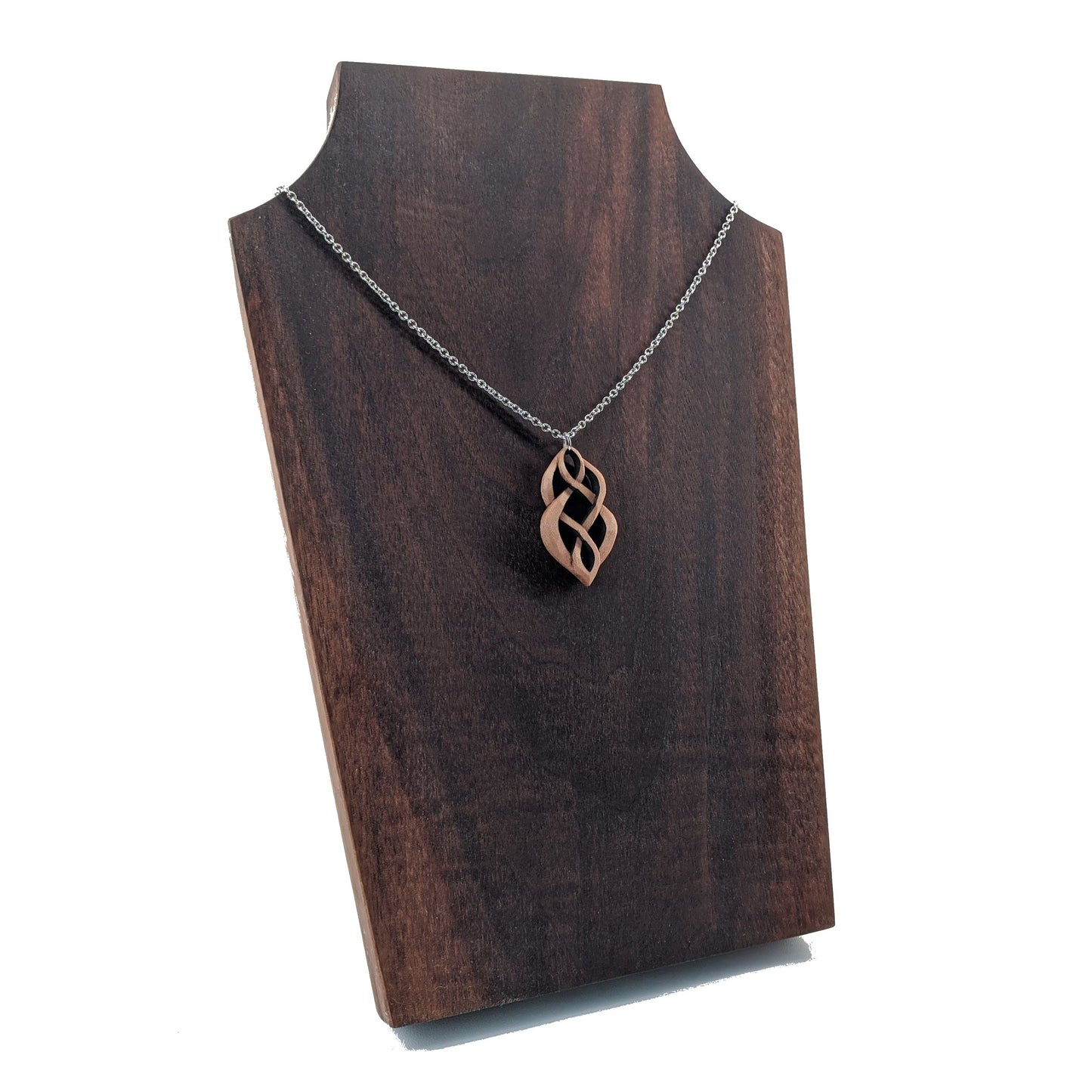 Wooden necklace pendant carved so that curving shapes weave into each other. Made from hard maple wood and hanging from a silver chain against a dark walnut background.