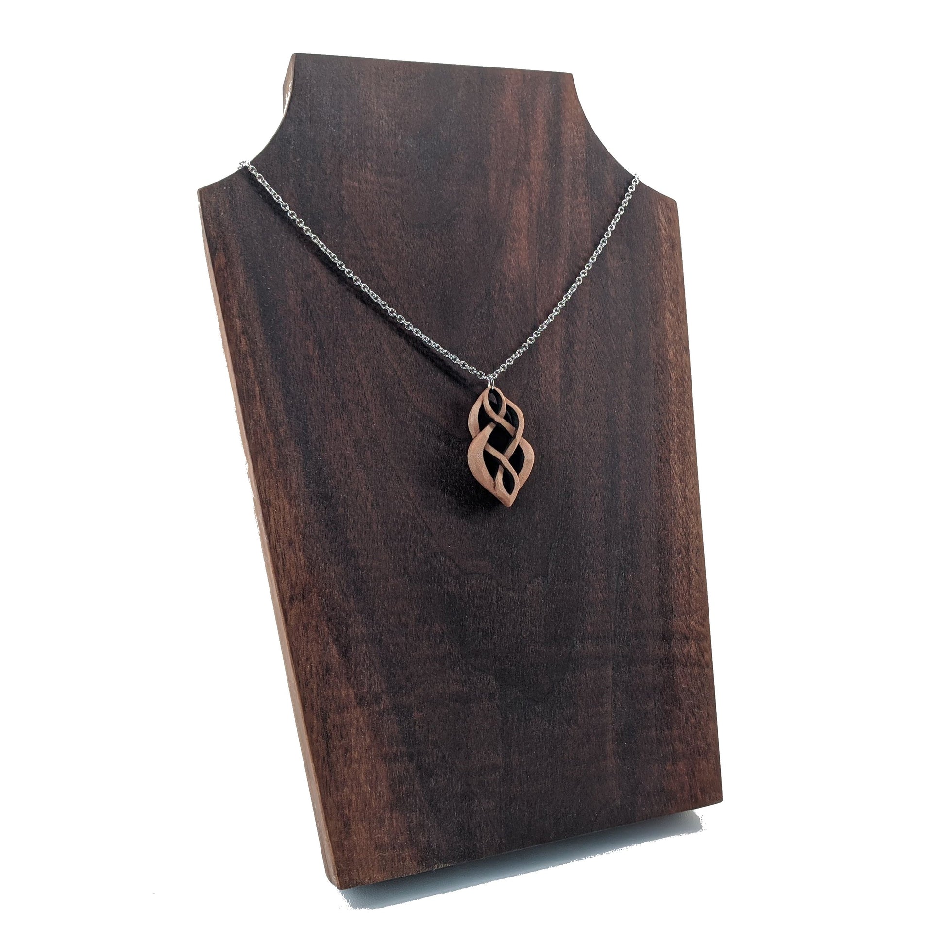 Wooden necklace pendant carved so that curving shapes weave into each other. Made from hard maple wood and hanging from a silver chain against a dark walnut background.