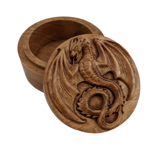 Round wooden box 3D carved with a mediaeval dragon with pointed wings spread, horned head, open mouth and serpentine tongue. It has scales down its belly and spines all down its back. Made from hard maple wood stained brown against a white background