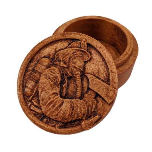 Round wooden box 3D carved with a firefighter in full gear with hat, oxygen tank, mask on and axe in hand within a fire hose border in front of a background of flames. Made from hard maple wood with a brown stain against a white background