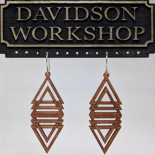 Pair of wooden earrings with silver stainless steel hooks. They are multiple brown triangles overlapping and mirrored to make a diamond shape. Made from birch wood hanging from a model Davidson Workshop sign against a white background (Close up View)