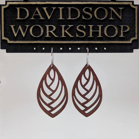 Pair of wooden earrings with silver stainless steel hooks. They are brown almond shaped with a herringbone style cutout within. Made from birch wood hanging from a model Davidson Workshop sign against a white background. (Close up View)