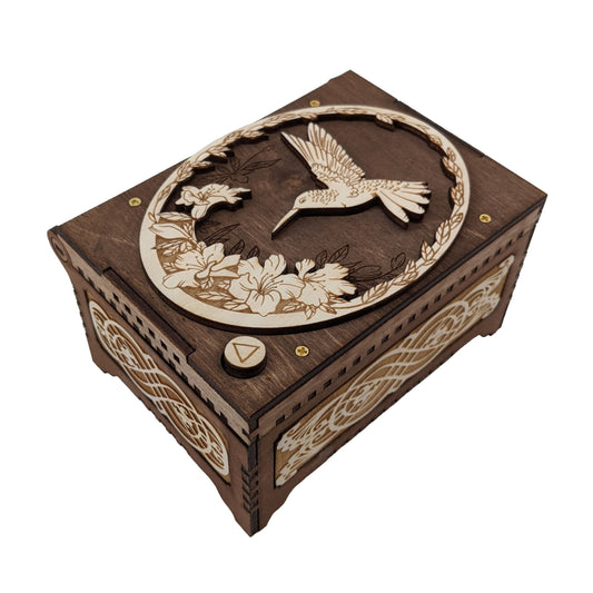 Hummingbird music box, dark brown and birch wood in color, with decorative floral filigree patterns engraved on the sides.