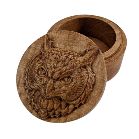 Round wooden box 3D carved with an owl face looking forward with a fierce expression. It has pointed ears and bushy feathers around its face and finer ones around its eyes and mouth. Made from hard maple wood stained brown against a white background.