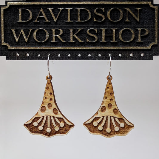 Pair of wooden earrings with silver stainless steel hooks. They are natural finish polka dotted petals with multiple pistols in their center. Made from birch wood hanging from a model Davidson Workshop sign against a white background. (Close up View)