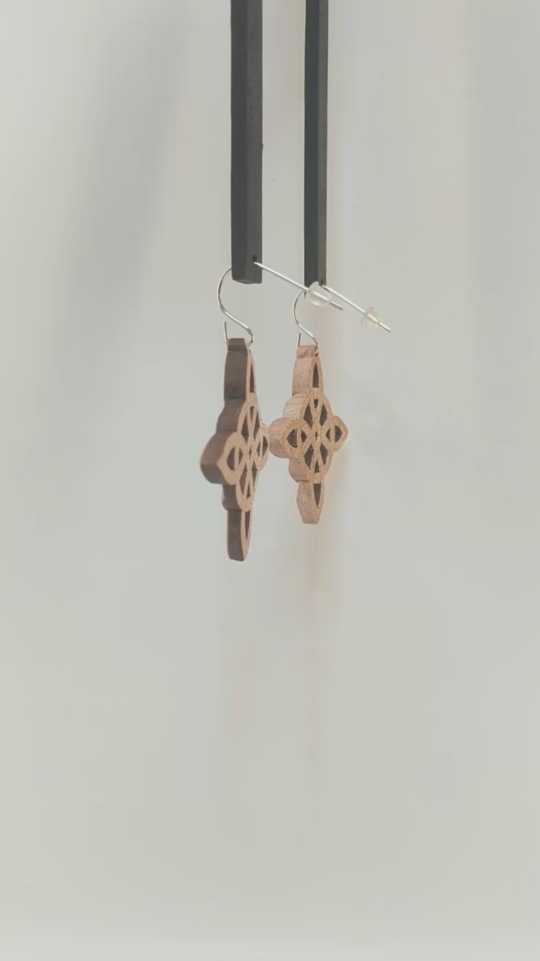 Pair of wooden earrings with silver stainless steel hooks. They are Celtic style crosses, carved in a woven pattern with a circle center. Made from hard maple hanging and rotating against a white background.