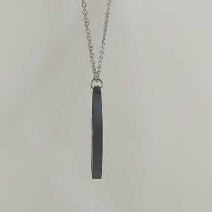 Wooden necklace pendant cut into a teardrop shape with a chevron pattern cut throughout it. Made from dark walnut and hanging from a silver stainless steel chain against a white background rotating on a table.