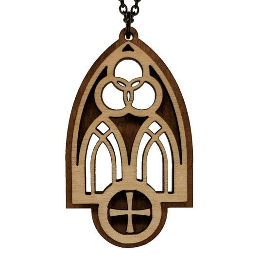 Wooden necklace pendant inspired by a gothic church window. includes a trinity symbol above and a cross below. Made from two layers, dark and light birch wood. Hanging from a black stainless steel chain against a white background.