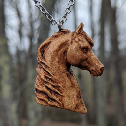 Wooden pendant realistically carved in the shape of a horse. Made form hard maple and hung from a silver stainless steel chain against a forest background.