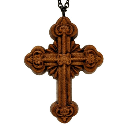 Wooden necklace pendant carved in the shape of an ornate cross. Made from hard maple wood and hanging from a black stainless steel chain against a white background.