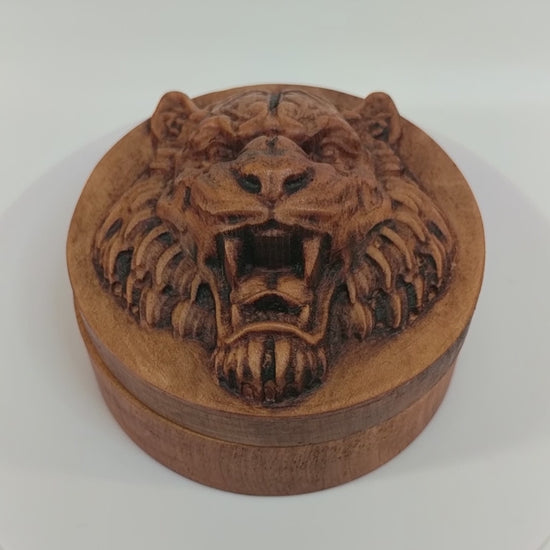 Round wooden box 3D carved with a tigers face looking straight ahead scowling and and showing its large fangs. It has burly fur on the sides of its face and chin. Made from hard maple wood stained brown against a white background rotating on a table.
