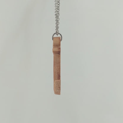 Wooden pendant necklace carved in the shape of a anchor. Made from hard maple wood. It hangs from a black stainless steel chain against a white background rotating on a table.