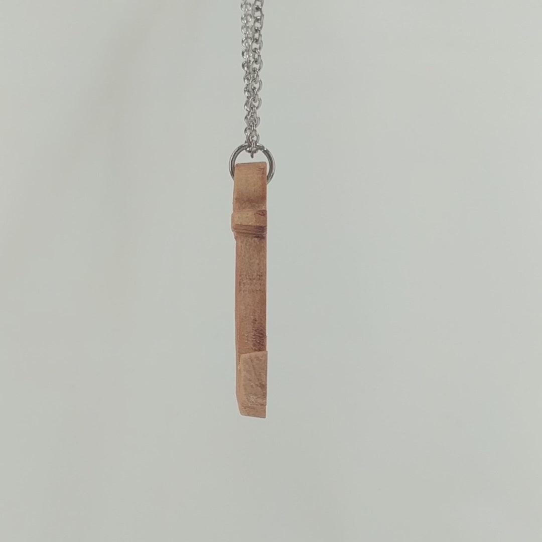 Wooden pendant necklace carved in the shape of a anchor. Made from hard maple wood. It hangs from a black stainless steel chain against a white background rotating on a table.