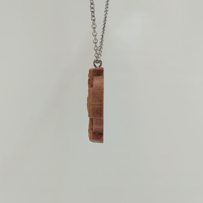 Wooden necklace pendant created in the shape of a Celtic cross. Made from hard maple wood and hanging from a black stainless steel chain against a white background rotating on a table.