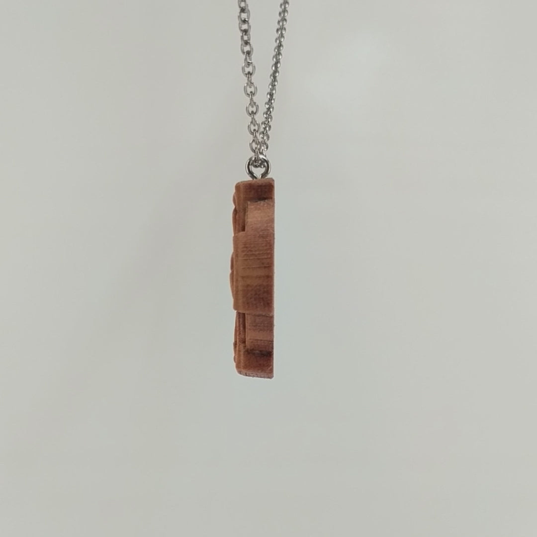 Wooden necklace pendant created in the shape of a Celtic cross. Made from hard maple wood and hanging from a black stainless steel chain against a white background rotating on a table.