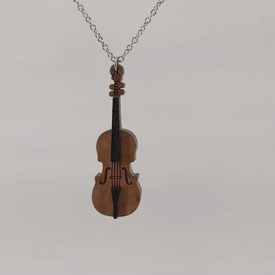 Wooden necklace pendant created in the shape of a miniature cello stand of bass. Made from cherry wood. Hanging and rotating from a silver stainless steel chain against a white background.