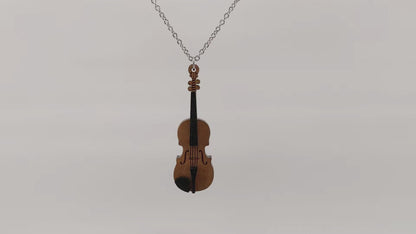 Wooden necklace pendant created in the shape of a miniature violin. Made from hard maple wood. Hanging and rotating from a silver stainless steel chain against a white background.