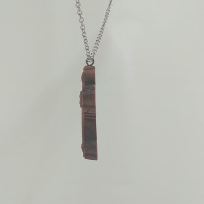 Wooden necklace pendant carved in the shape of an ornate cross. Made from hard maple wood and hanging from a silver stainless steel chain against a white background rotating on a table.