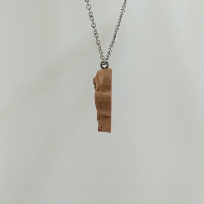 Wooden necklace pendant carved in the shape of a skull with a snake crawling through the eyes. Made from hard maple wood and hanging from a silver stainless steel chain against a white background rotating on a table. 