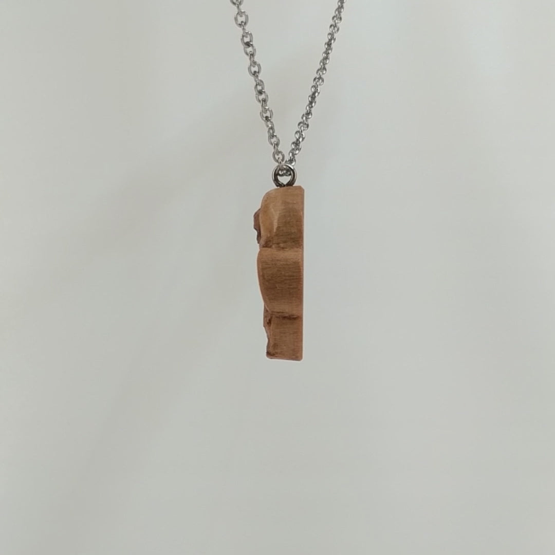 Wooden necklace pendant carved in the shape of a skull with a snake crawling through the eyes. Made from hard maple wood and hanging from a silver stainless steel chain against a white background rotating on a table. 