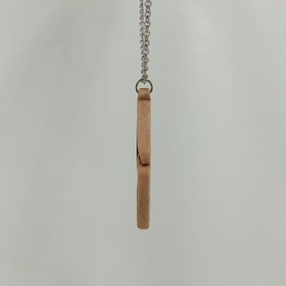 Wooden necklace pendant carved so that curving shapes weave into each other. Made from hard maple wood and hanging from a silver chain against a white background rotating on a table. 