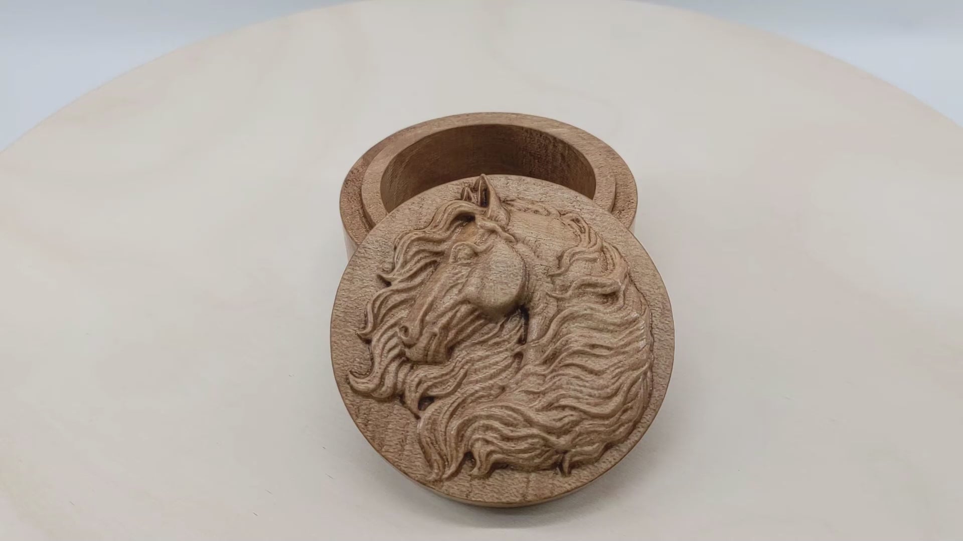 Round wooden box 3D carved with a horse face and neck looking to the left. The horse has long hair flowing from behind its face and down its neck. Made from hard maple wood stained brown against a white background rotating on a table.