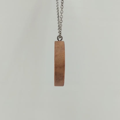 Round wooden necklace pendant carved in the shape of two hands reaching out to touch each other. Made from hard maple wood. Hanging from a silver stainless steel chain against a white background rotating on a table.