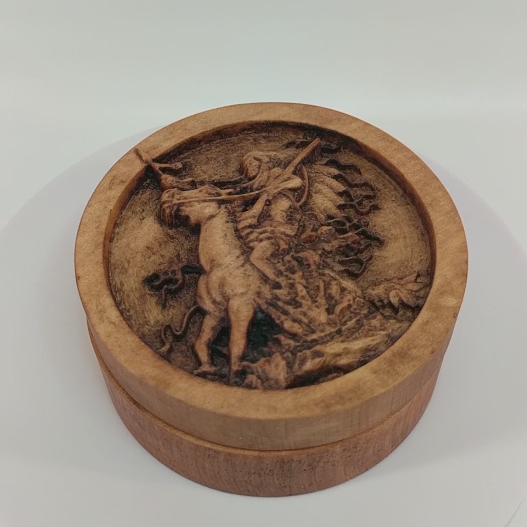 Round wooden box 3D carved with a native american warrior on horse rearing up in some shrubbery. Has big headdress. Holding reins and gun shouldered in one hand, spear in the other. Made from hard maple wood stained brown against a white background rotating on a table.