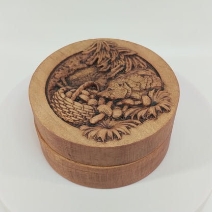 Round wooden box 3D carved with a hedgehog getting into a basket of mushrooms. Surrounded with flowers and leaves on the forest floor and eating the spilled mushrooms. Made from hard maple wood stained brown against a white background rotating on a table.