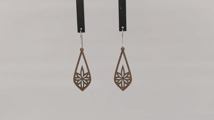 Pair of wooden earrings with silver stainless steel hooks. They are long brown teardrops with an 8 pointed star with sharp points within. Made from birch wood hanging and rotating against a white background.