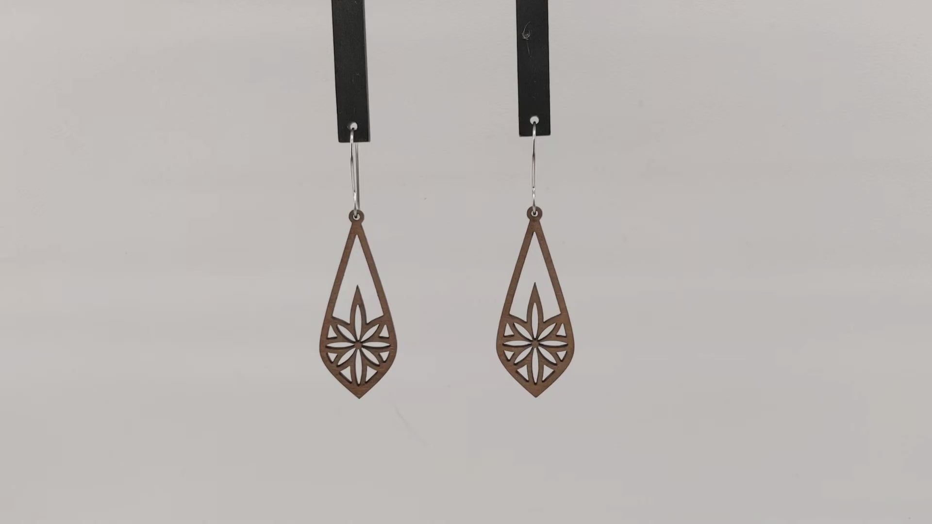 Pair of wooden earrings with silver stainless steel hooks. They are long brown teardrops with an 8 pointed star with sharp points within. Made from birch wood hanging and rotating against a white background.