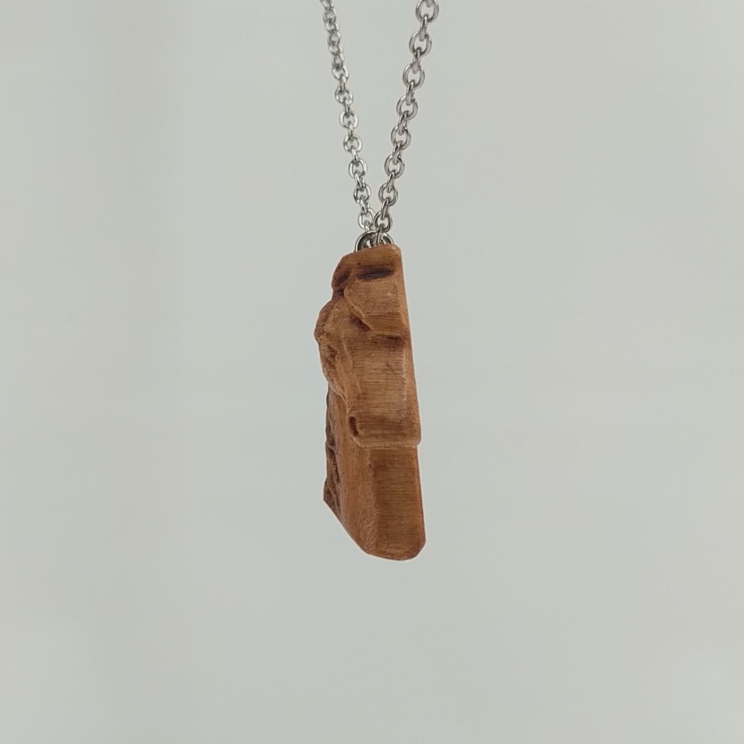 Wooden pendant realistically carved in the shape of a horse. Made form hard maple and hung from a silver stainless steel chain against a white background rotating on a table.