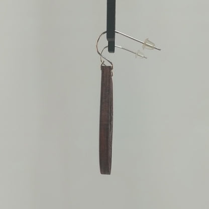 Pair of wooden earrings with silver stainless steel hooks. They are brown teardrop shaped with a woven pattern within and a tear in the center. Made from birch wood hanging and rotating against a white background.