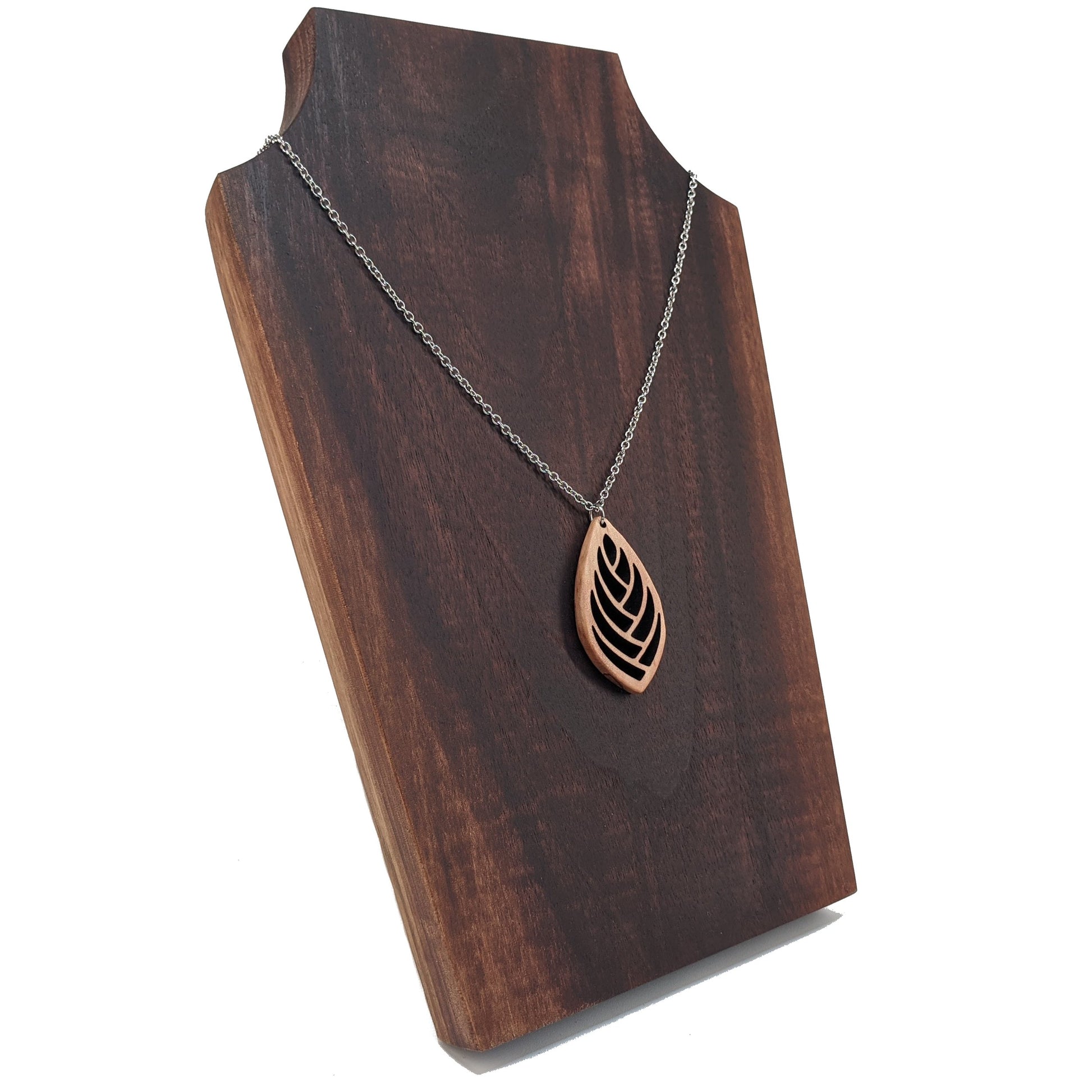 Wooden necklace pendant cut into a teardrop shape with a herring bone pattern cut throughout it. Made from hard maple and hanging from a silver stainless steel chain against a cherry wood background.