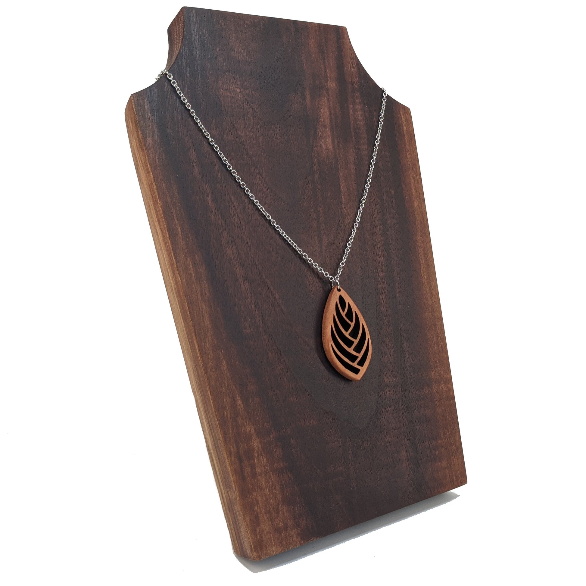 Wooden necklace pendant cut into a teardrop shape with a herring bone pattern cut throughout it. Made from cherry and hanging from a silver stainless steel chain against a dark walnut background.