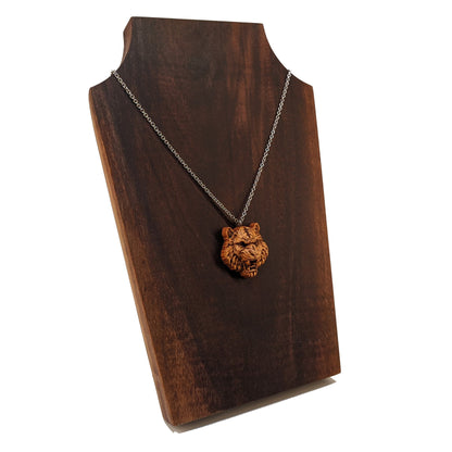 Wooden pendant necklace carved in the shape of tigers head. Made from hard maple and hanging from a silver stainless steel chain against a dark walnut background.