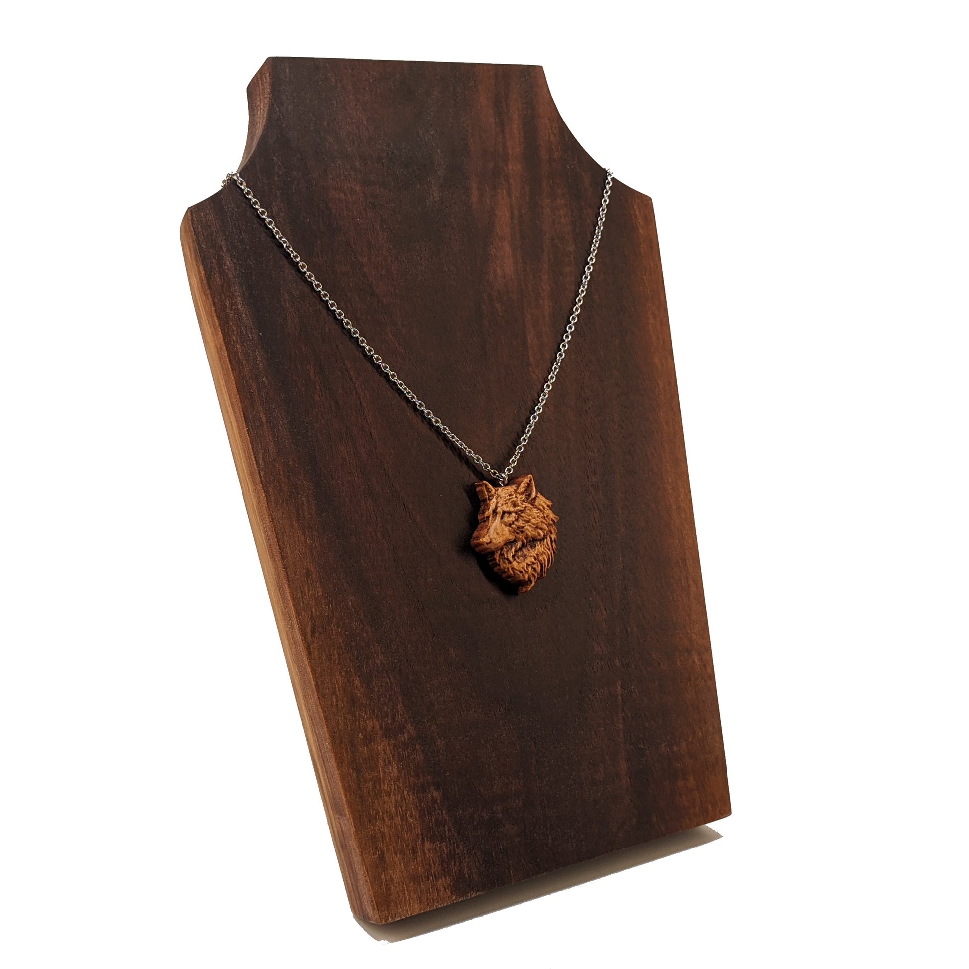 Wooden pendant necklace carved in the shape of a wolf head. The wolf faced to the side and made from hard maple wood. It hangs from a silver stainless steel chain against a dark walnut background.